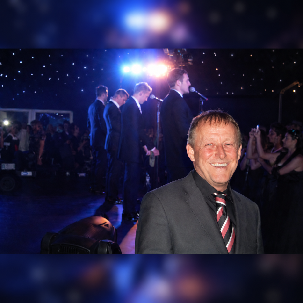 Dave smiling while Westlife perform live