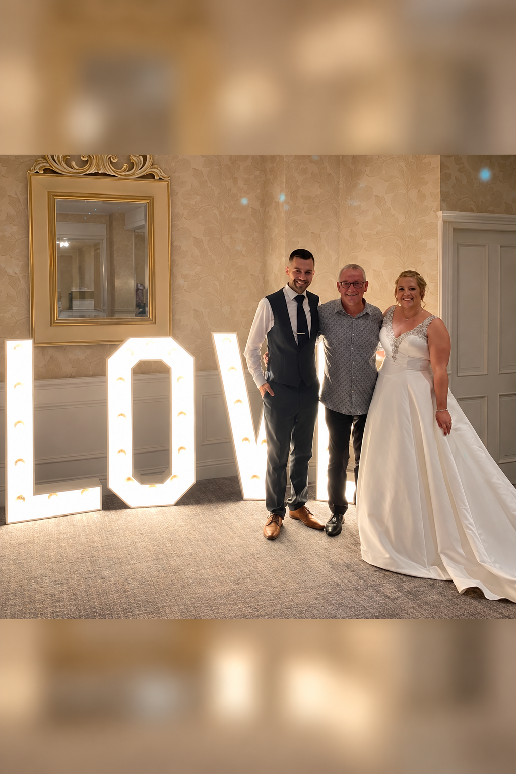Dave with a bride and groom beside illuminated LOVE letters